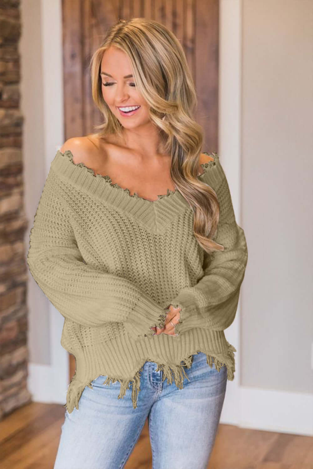 Woman wearing Bella Road frayed hem dropped shoulder sweater in cozy room, showcasing stylish and playful fashion.