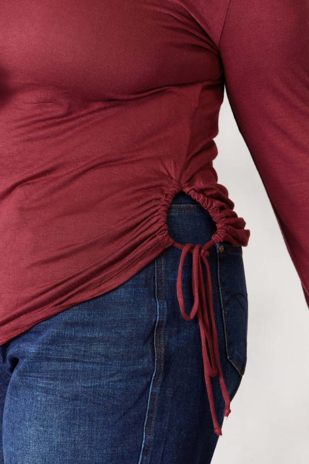 Close-up of drawstring detail on a maroon round neck long sleeve top with blue jeans