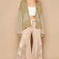 Trendy woman in a green distressed hem hooded cardigan paired with stylish cream wide-leg pants and sneakers.