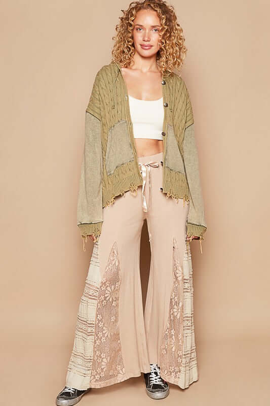 Trendy woman in a green distressed hem hooded cardigan paired with stylish cream wide-leg pants and sneakers.