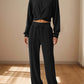 Woman wearing Bella Road Crisscross Round Neck Top and Drawstring Pants Set in black, standing in a sunlit room.