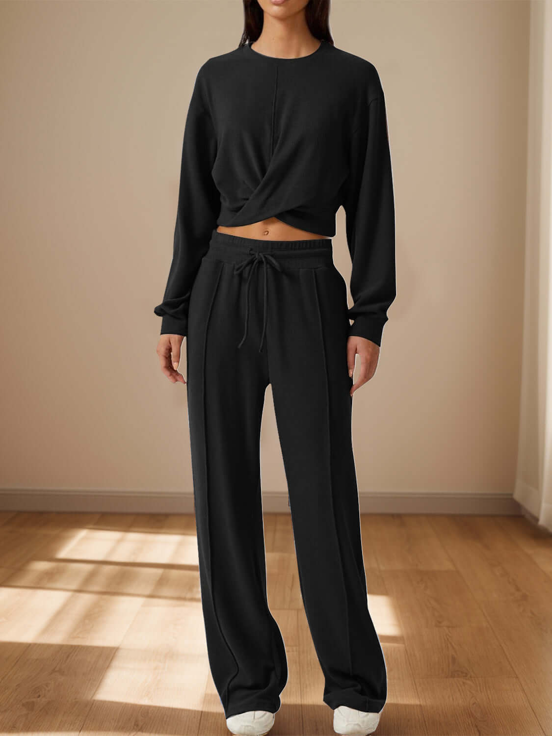 Woman wearing Bella Road Crisscross Round Neck Top and Drawstring Pants Set in black, standing in a sunlit room.