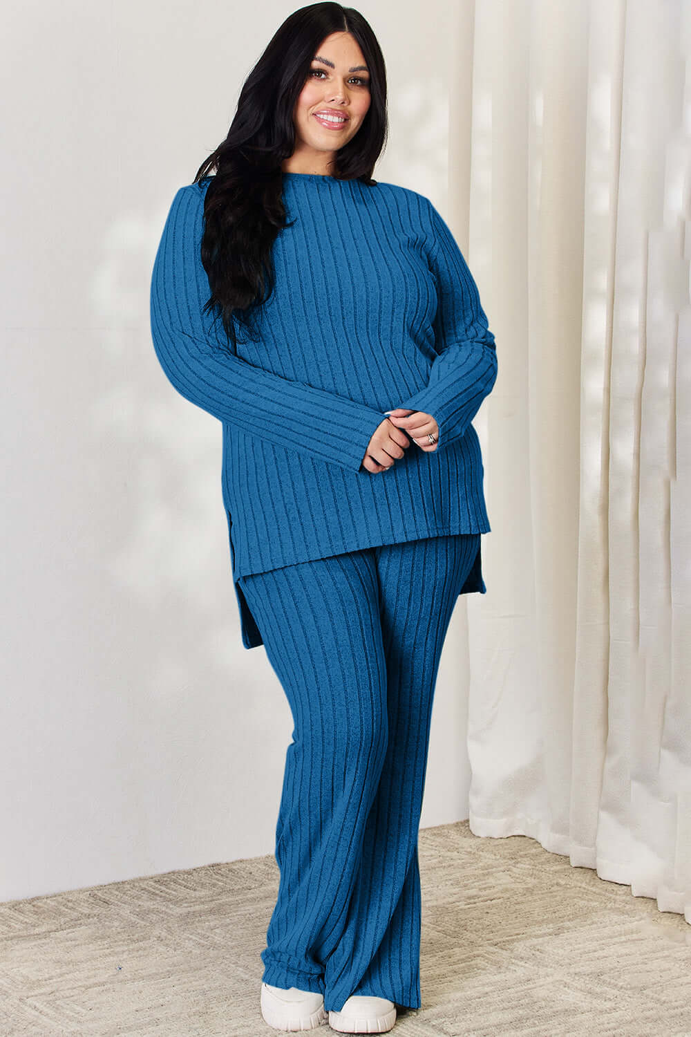 Curve model wearing blue ribbed high-low top and wide leg pants set, slightly stretchy two-piece outfit made of polyester and elastane.