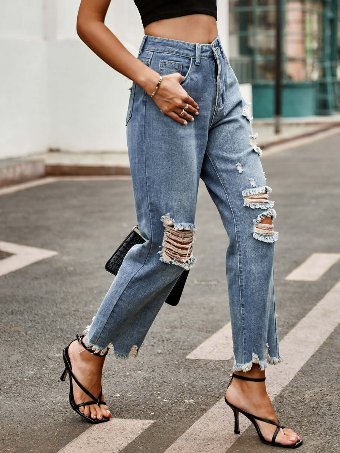 Woman wearing Bella Road Distressed Raw Hem Jeans with Pockets, styled with strappy heels and a black top, walking on a street.