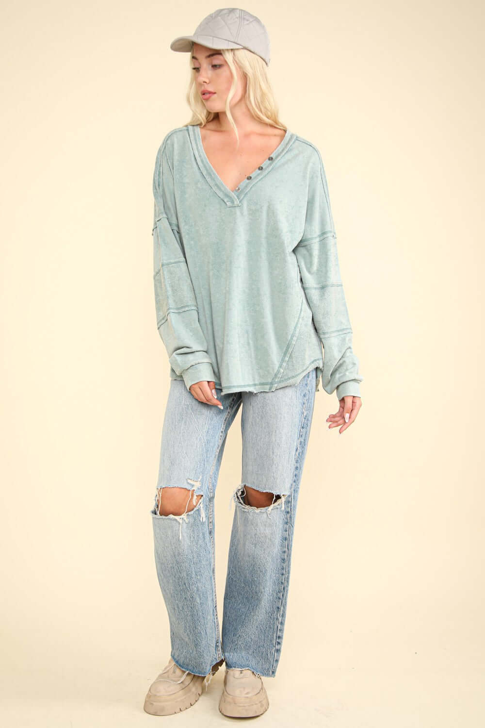 Woman wearing VERY J Washed V-Neck Exposed Seam Knit Top with long sleeves, drop shoulder design, and distressed jeans.