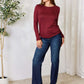 Woman wearing a burgundy drawstring round neck long sleeve top paired with blue jeans, posing in a stylish indoor setting.