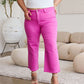 Woman wearing high-waisted pink cropped jeans with raw hem and white tank top standing in stylish living room