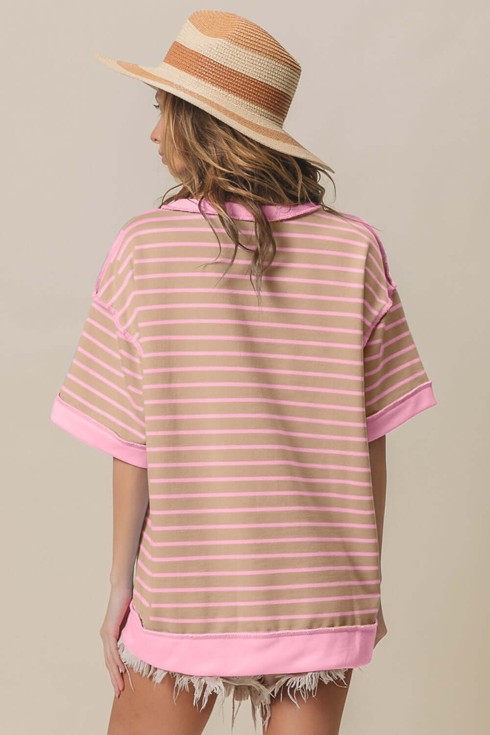 Woman wearing Exposed Seam Stripe Contrast T-Shirt in pink and white with straw hat and distressed shorts. Back view.