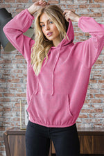 Woman wearing a stylish urban ribbed long sleeve hoodie with a drawstring hood and kangaroo pocket in a casual home setting