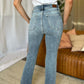 Woman wearing Judy Blue medium rise bootcut jeans in a living room setting.