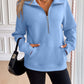 Woman wearing a light blue Ivy Lane Half Zip Raglan Sleeve Sweatshirt with black shorts carrying a black handbag in a stylish room