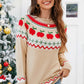 Woman wearing angel wings graphic sweater with apple design, round neck, and long sleeves, standing beside a decorated Christmas tree.