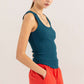 Woman wearing teal ribbed scoop neck racerback tank top with red pants, showcasing a sporty and chic aesthetic.