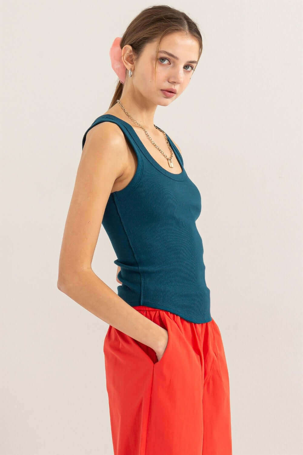 Woman wearing teal ribbed scoop neck racerback tank top with red pants, showcasing a sporty and chic aesthetic.