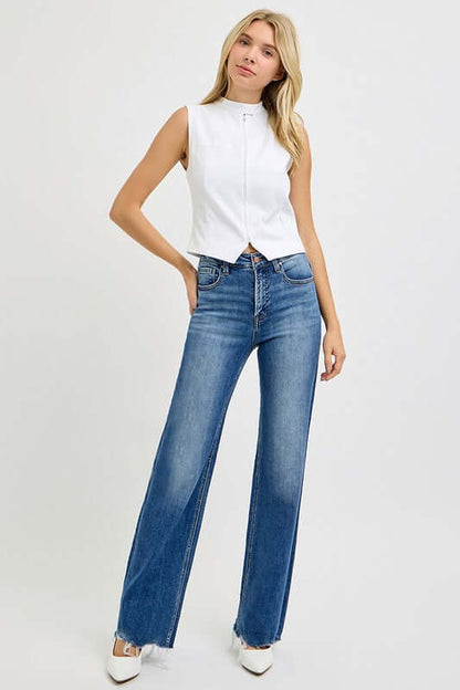 Model showcasing RISEN tummy control high rise raw cut jeans with a fitted white top and stylish heels.