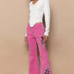 Stylish model in pink raw hem embroidered flare pants paired with a chic white top, showcasing a bohemian flair.