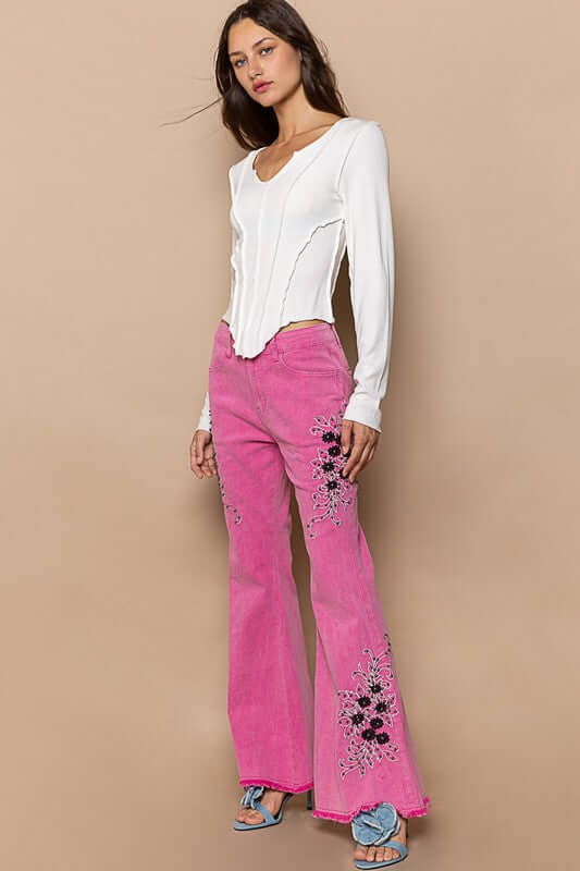 Stylish model in pink raw hem embroidered flare pants paired with a chic white top, showcasing a bohemian flair.