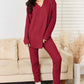 Woman wearing a notched long sleeve top and pants set in red, ribbed fabric, slightly stretchy, 96% polyester and 4% elastane, standing in modern living room