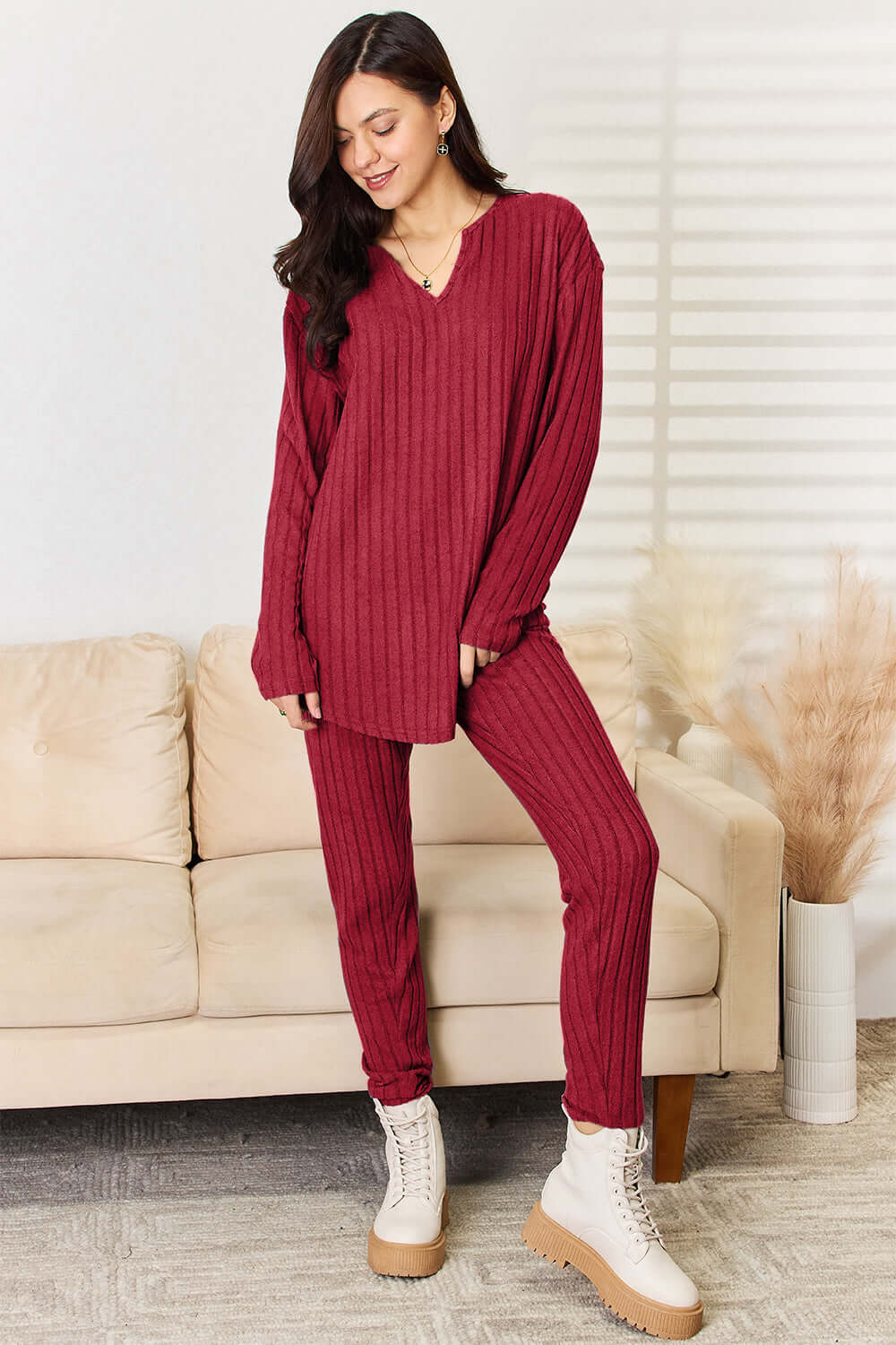 Woman wearing a notched long sleeve top and pants set in red, ribbed fabric, slightly stretchy, 96% polyester and 4% elastane, standing in modern living room