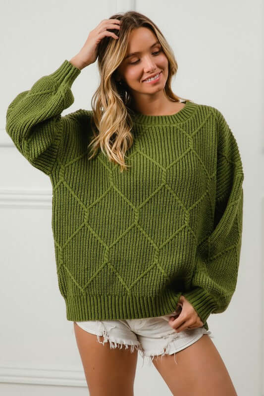 Model wearing a green BiBi diamond texture round neck long sleeve sweater styled with white shorts, showcasing casual elegance.