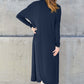 Woman wearing navy open front long sleeve cover up from the back, standing against concrete wall.