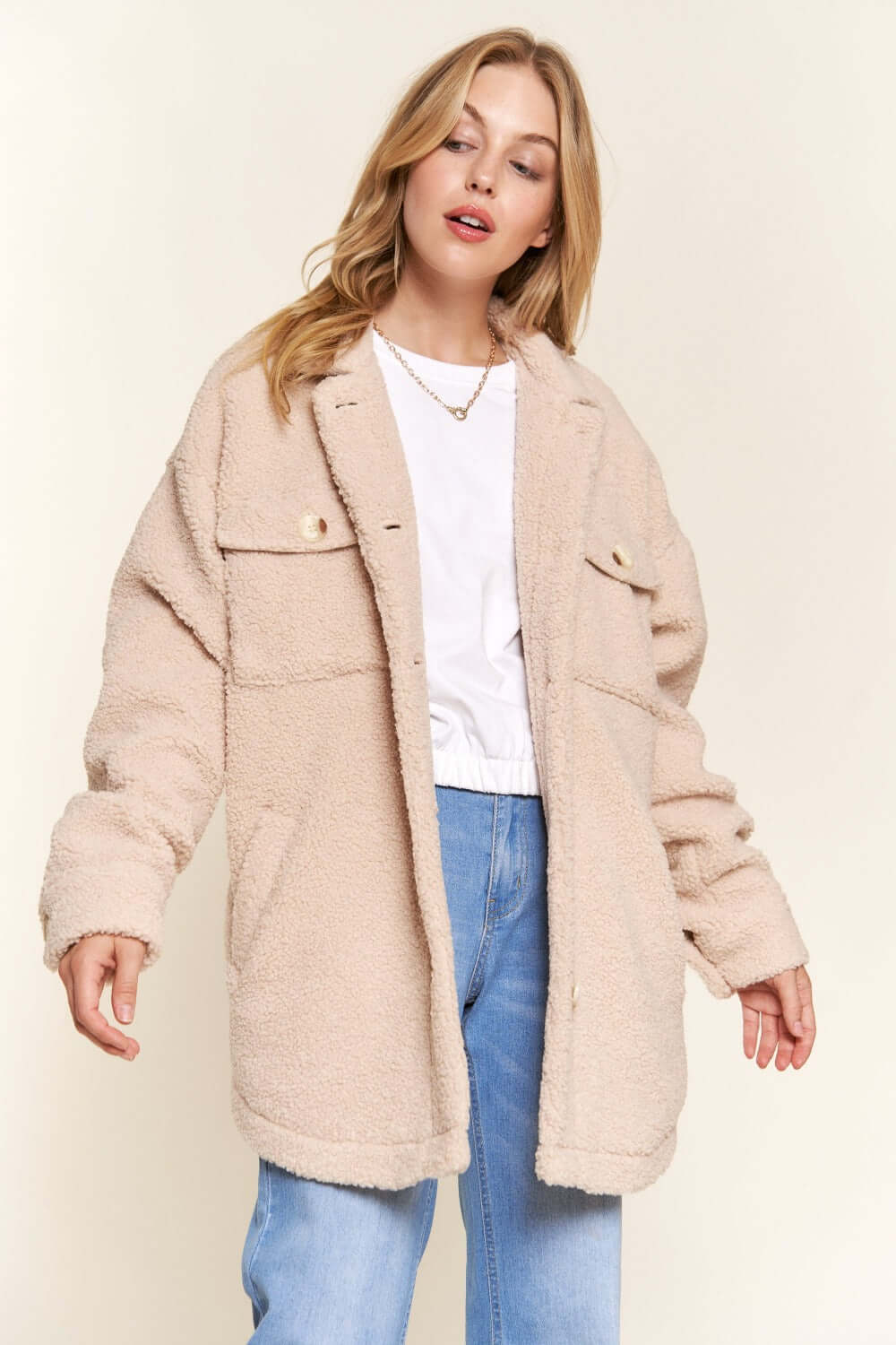 Woman wearing a cozy teddy sherpa button-down shacket with curved hem, paired with a white top and jeans, showcasing casual style.