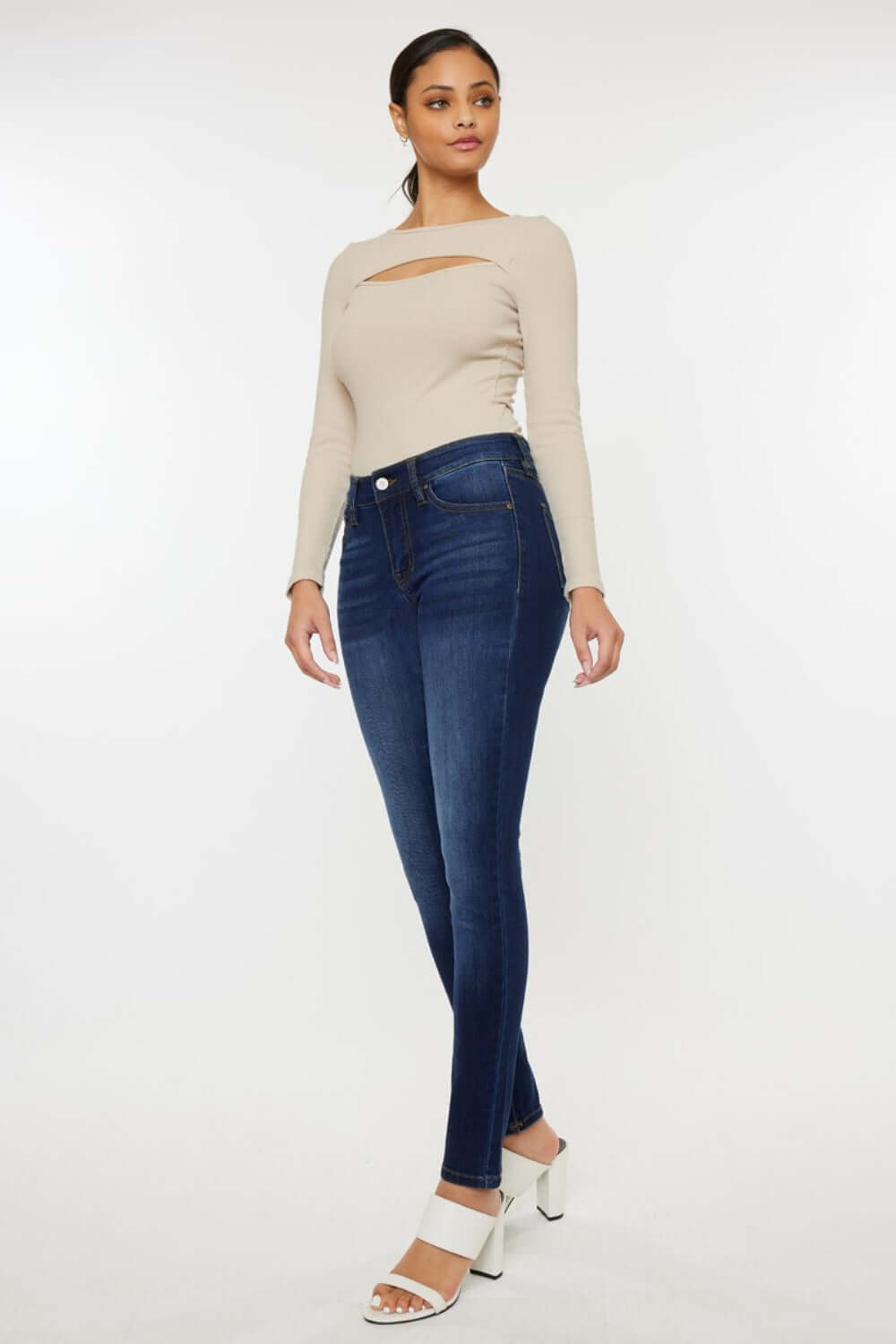 Woman wearing mid rise gradient skinny jeans with a stylish beige top and white heels.