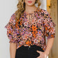 Woman wearing a Floral Tie Neck Ruffled Blouse with charming floral print and ruffled details, paired with black jeans.