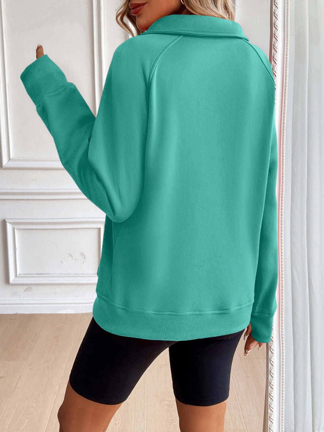 Woman wearing Ivy Lane Half Zip Raglan Sleeve Sweatshirt in teal color, showing back view.