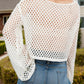 Sheer cream openwork cover up with long sleeves, styled with denim shorts for a chic beach look.