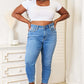 Woman wearing high waist skinny jeans in medium ash wash, paired with a white crop top and brown boots, posing confidently indoors.