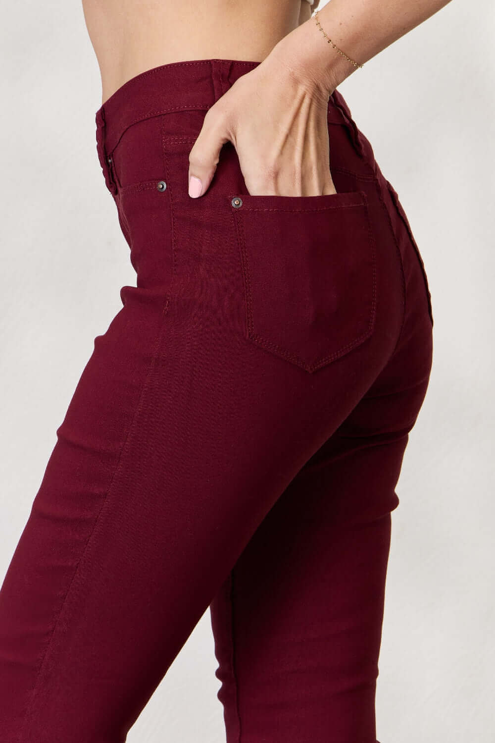 Woman wearing Hyperstretch Mid-Rise Skinny Jeans by YMI Jeans in deep burgundy, showing back pocket detail for a stylish and comfortable fit.