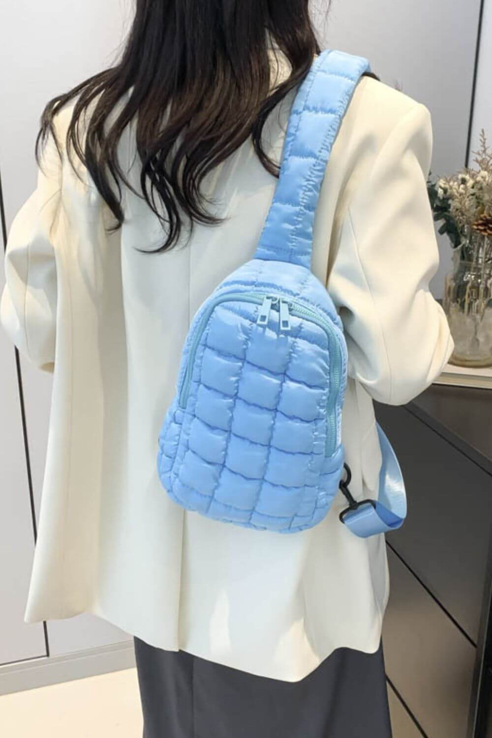 Woman in white coat wearing blue quilted nylon crossbody bag with a stylish puffy design.