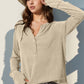 Woman wearing a Double Take Full Size Notched Thumbhole Long Sleeve T-Shirt in beige, paired with a stylish hat and white pants.