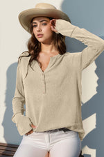 Woman wearing a Double Take Full Size Notched Thumbhole Long Sleeve T-Shirt in beige, paired with a stylish hat and white pants.