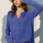 Woman wearing blue full size notched thumbhole long sleeve t-shirt with hat and white pants