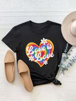 Black graphic round neck short sleeve T-shirt with "Love is Love" rainbow heart design, paired with tan shoes and a hat.