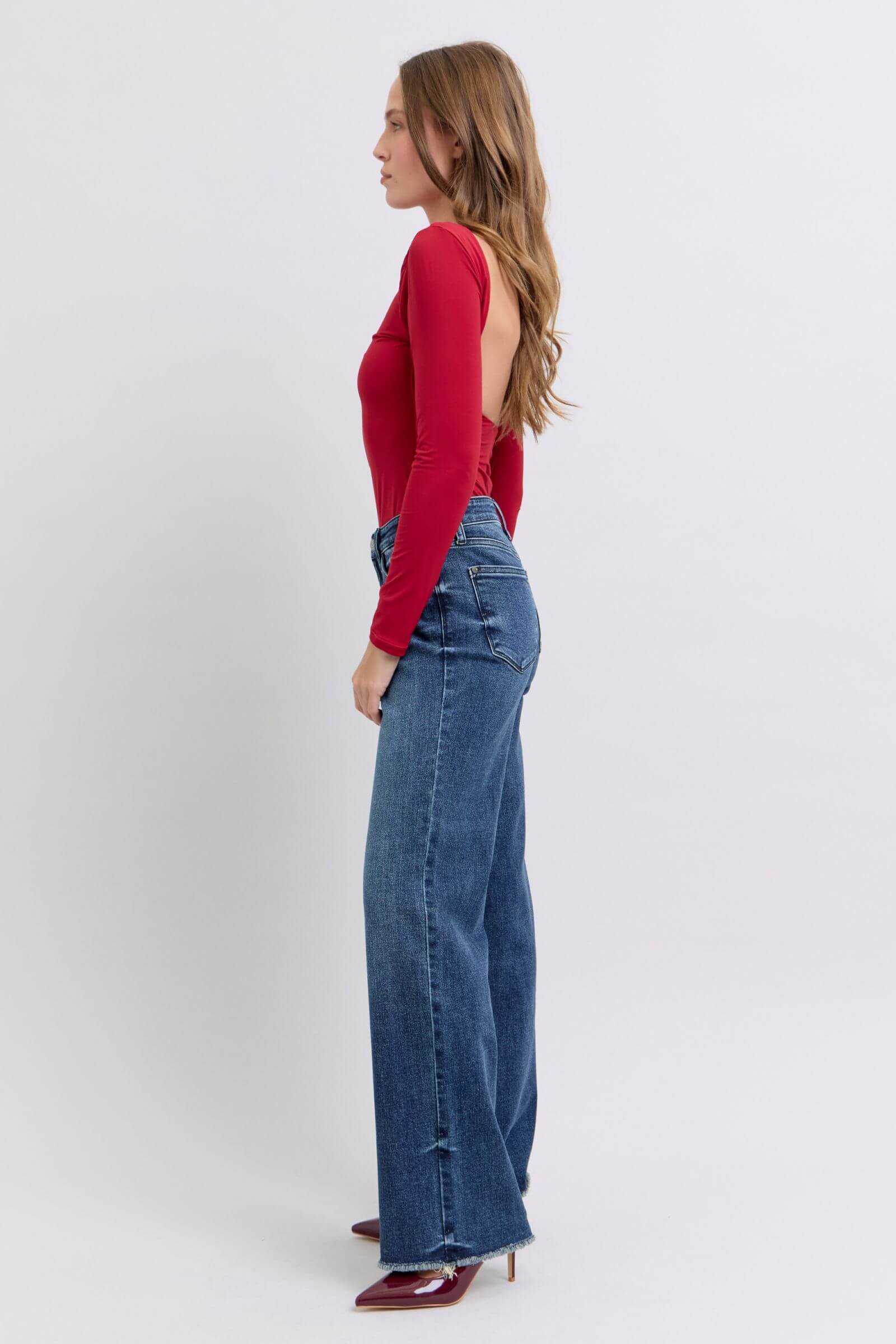 Model showcasing Judy Blue full-size raw hem mid-rise jeans in a stylish, relaxed fit with a red top.