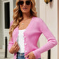 Woman wearing Bella Road Button Up Long Sleeve Cardigan in stylish pink, paired with sunglasses, white top, and blue jeans standing outside.