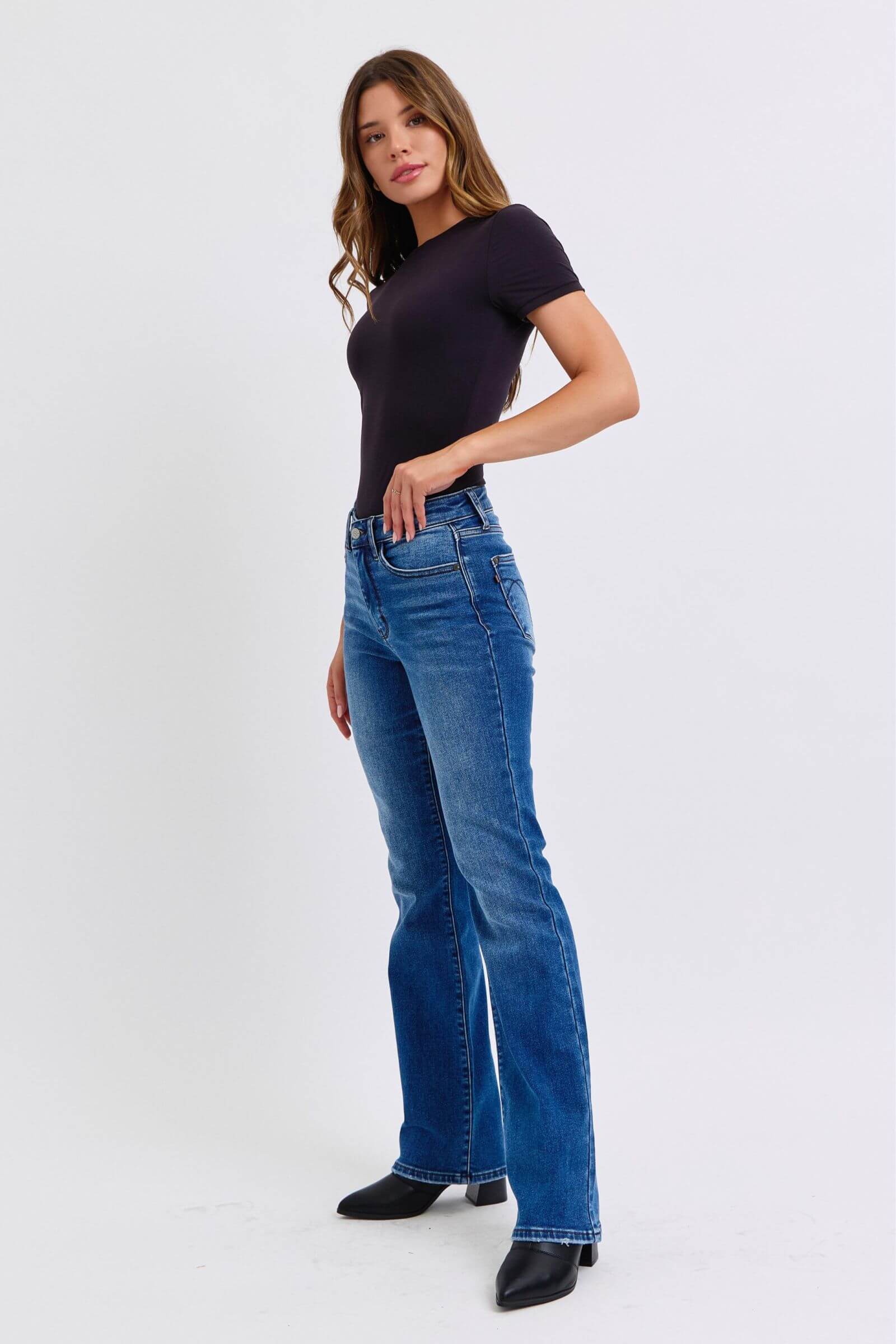 Model showcasing Judy Blue mid-rise bootcut jeans with thermal lining, styled in a chic black top and ankle boots.