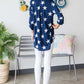 Woman wearing Heimish Roll-Tab Sleeve Star Print Top in navy with white stars, paired with white jeans and sandals, back view.