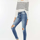 Woman modeling high waist distressed raw hem ankle skinny jeans, paired with a striped sweater and white sneakers. Trendy and edgy look.