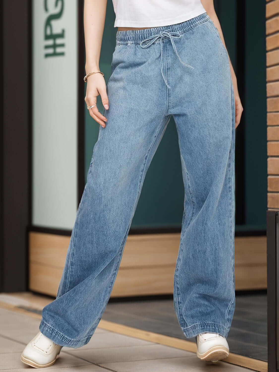 Woman wearing blue drawstring straight jeans with pockets and white shoes, standing outdoors.