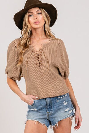 Stylish woman in a brown lace-up waffle knit crop top and denim shorts, accessorized with a wide-brim hat.