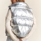 Trendy metallic puffer vest with snap and zipper closures for stylish warmth and easy layering.