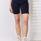 Woman wearing High Waist Tummy Control Bermuda Shorts from Judy Blue Jeans in dark blue with white boots.