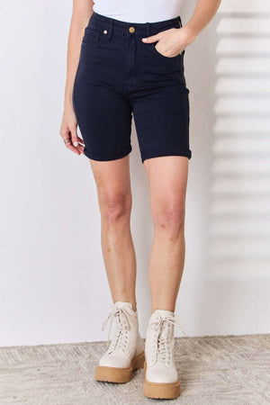 Woman wearing High Waist Tummy Control Bermuda Shorts from Judy Blue Jeans in dark blue with white boots.