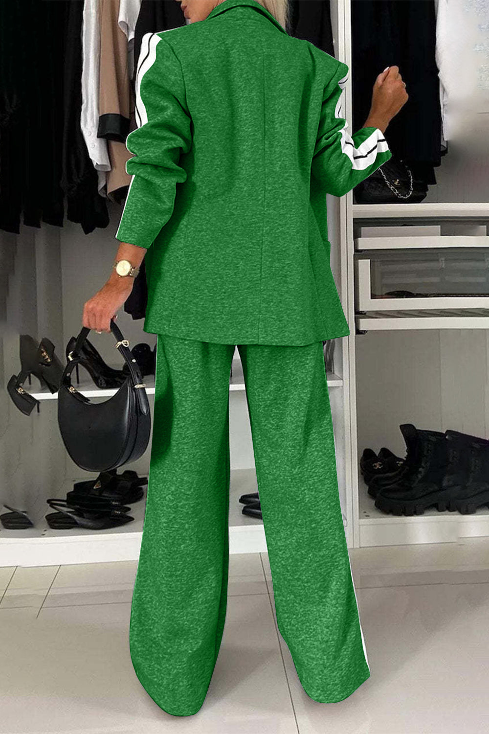 Woman in a green two-piece suit with white stripes, showcasing a stylish back view in a chic closet setting.