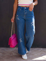 Woman wearing embroidered straight jeans with pockets, holding a pink handbag.