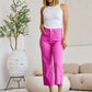 Woman wearing pink high-waist raw hem jeans and a white tank top standing in a stylish living room.